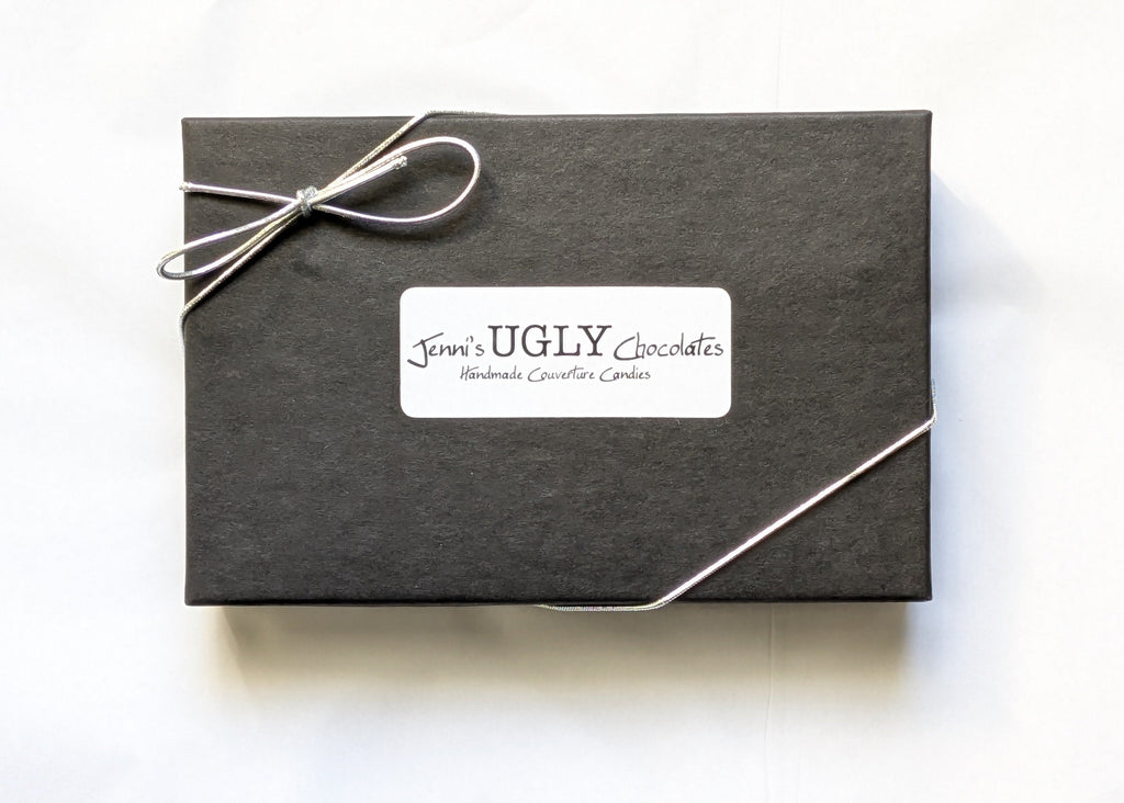 Black gift box with a white bow and 'Jewel's UGLY' label on a white background